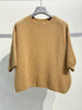 A camel-colored, oversized knit sweater—NOELINE’s 6004 kid mohair and wool sweater—is displayed on a hanger against a plain white wall.