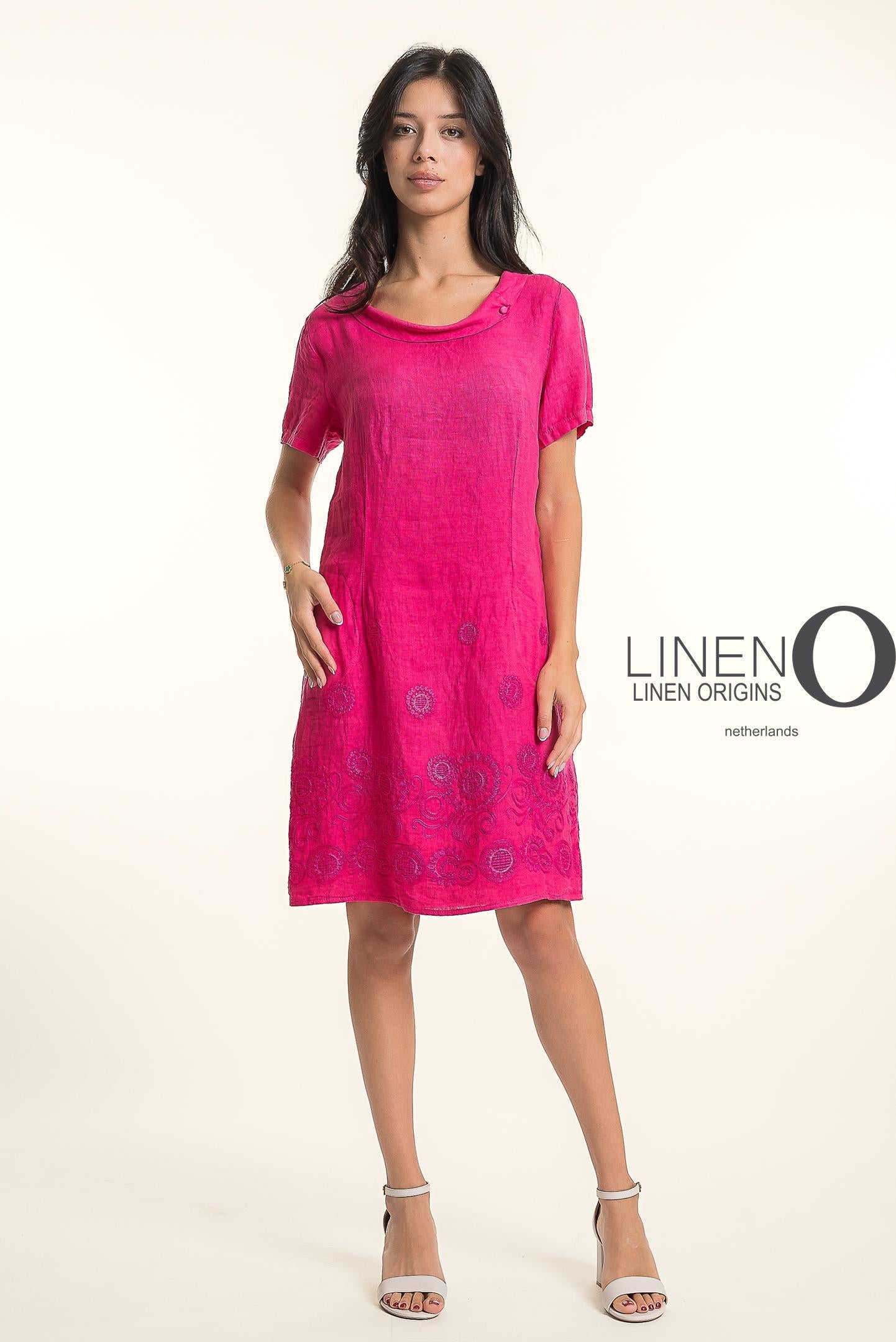 A woman in the LinenO French Linen Dress TP1745-43 Fuxia, featuring short sleeves and floral embroidery, poses confidently in white heels against a light background. "LINEN ORIGINS" appears beside her.