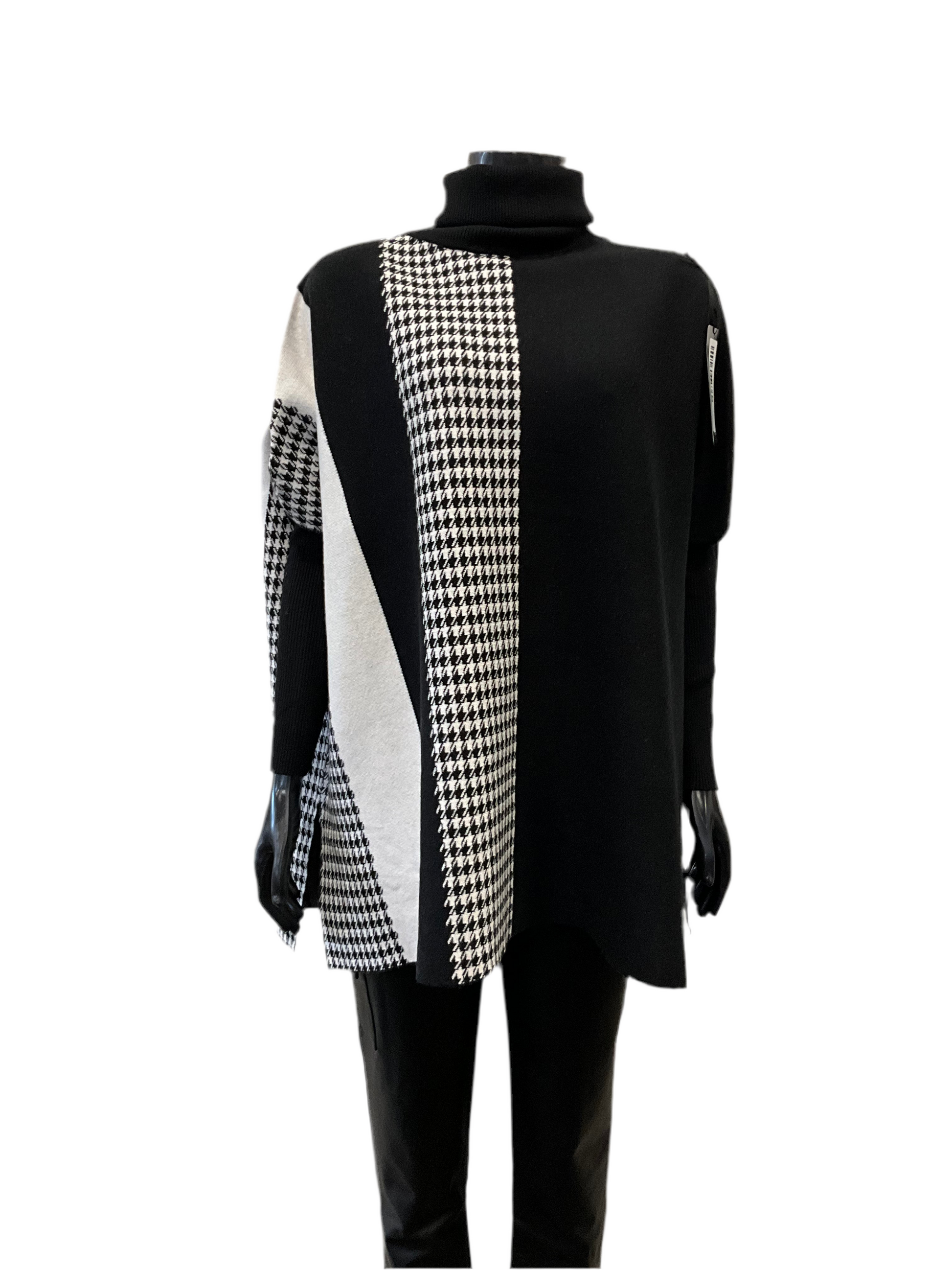 A black long-sleeve turtleneck sweater named "Full Coat Turtle Neck Black - Eternelle" from ETERNELLE, featuring a bold black-and-white geometric pattern with houndstooth and diagonal striped sections on the front. This luxurious top, made in Italy, is paired with black pants and showcased on a mannequin against a white background.
