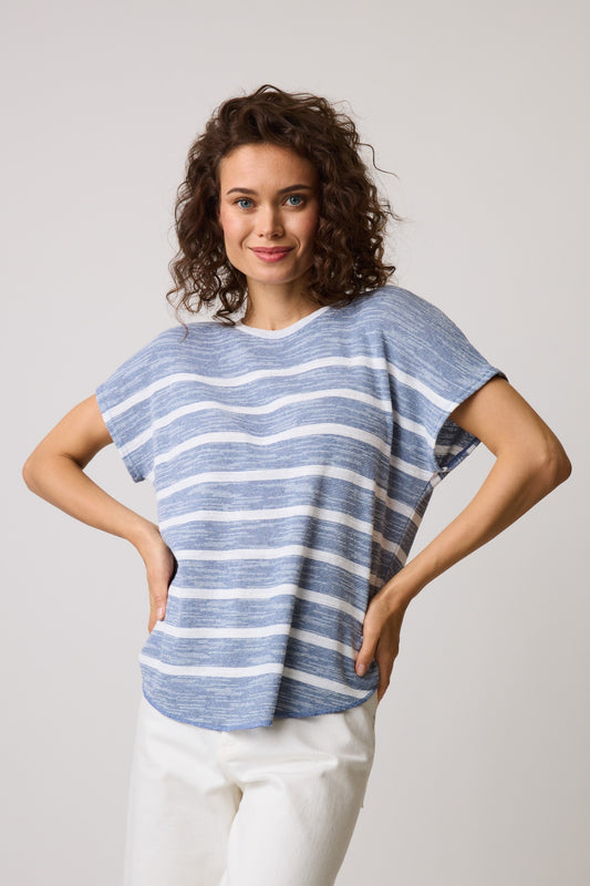 A person with curly hair smiles while wearing the Parkhurst Eco Stripe Short Sleeve 74907, made from sustainable materials, paired with white pants. They stand against a plain background with hands on hips.