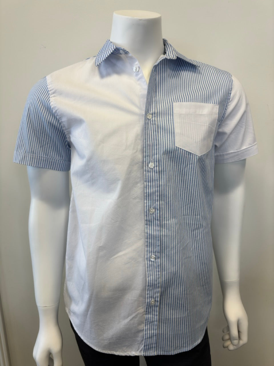 A mannequin showcases the Men’s Cotton Shirt - STRIPE WHITE/BLUE by Silver Jeans Co., which features a button-up style with alternating vertical white and blue stripes on the right side and pocket. The left side and sleeves are solid white, prominently displayed against a plain backdrop that accentuates the garment's unique design.