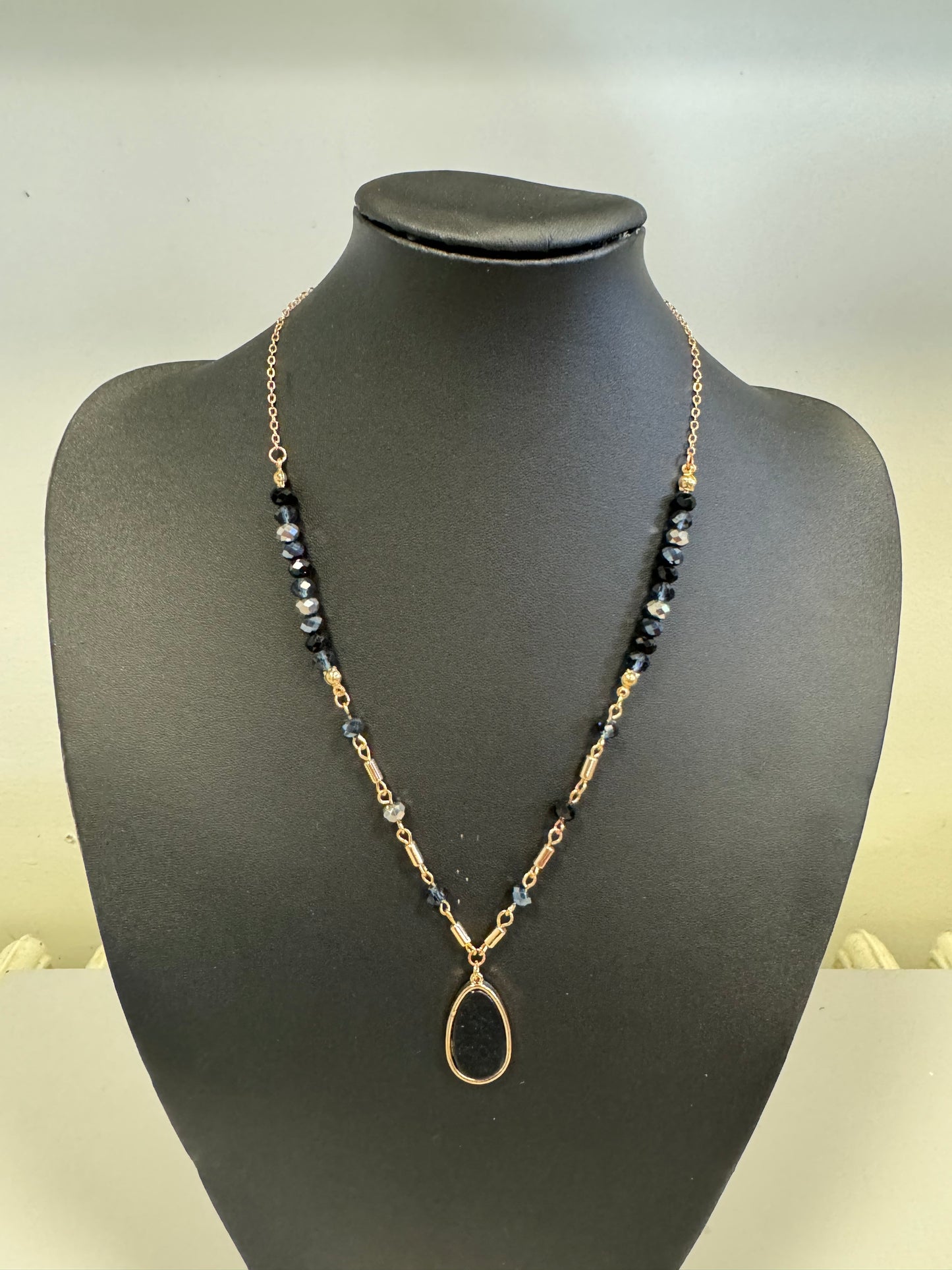 Showcased on a black bust, the Nina 1 Necklace by Elise Accessories features a chain with black beads and a prominent teardrop pendant that elegantly combines gold and silver elements. Its versatile design enhances any jewelry collection, making it stand out exquisitely against a neutral backdrop.