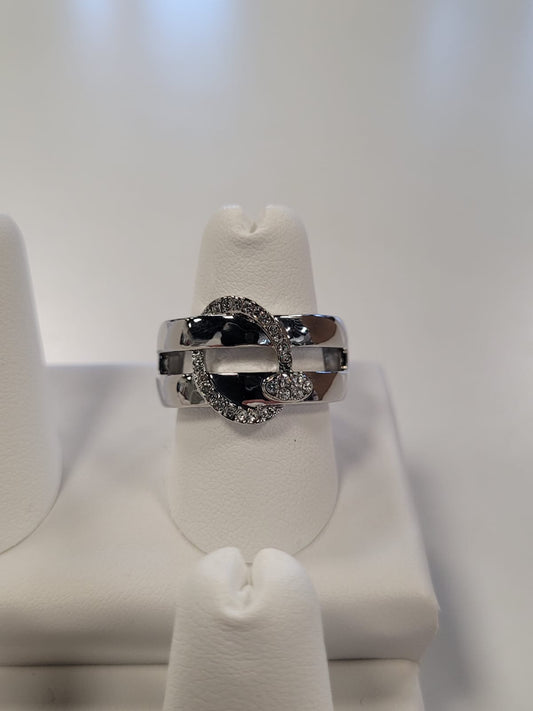 A shimmering Jenna-57 Adjustable Ring by Elise Accessories, showcasing a sophisticated silver finish with an oval-shaped, encrusted band design on top, is displayed vertically on a white ring stand. The background is blurred, accentuating the intricate details and sparkle of the elegant CZ-adorned ring.