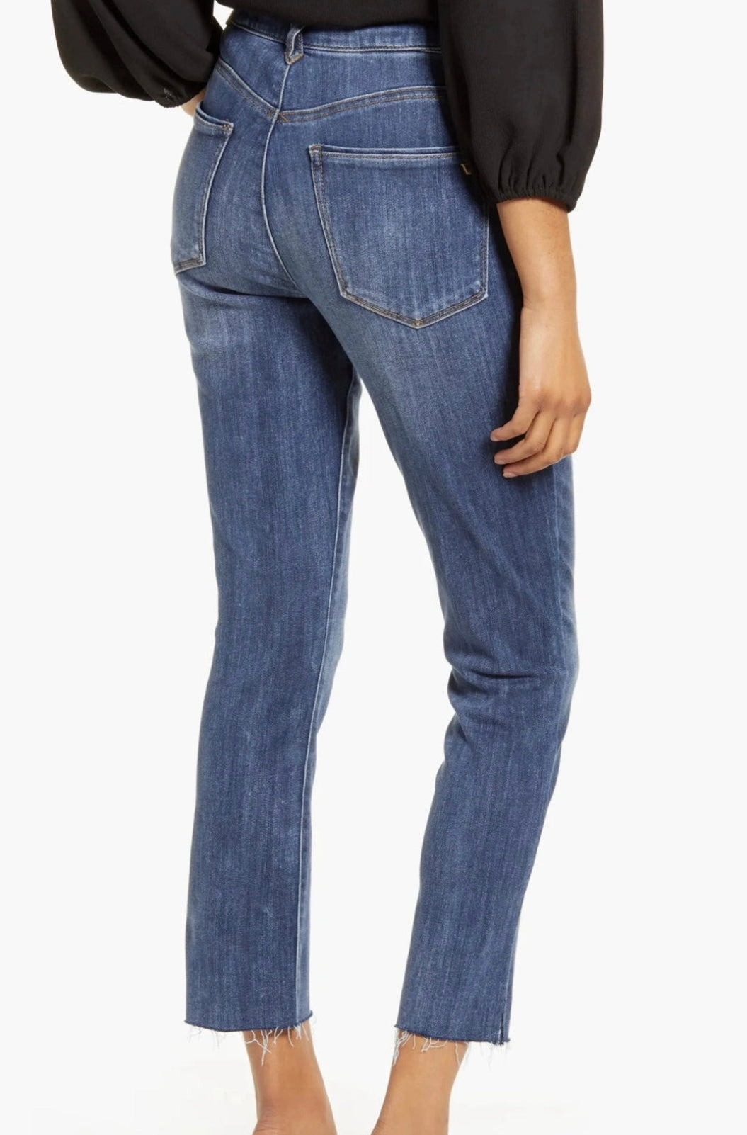 A person is wearing dark blue, slightly faded Logan Hi-Rise Skinny L1557KF8 jeans from Wit & Wisdom featuring a frayed hem and a black long-sleeve top. They are also sporting black high-heeled shoes. The image, which appears to be styled by Nordstrom, focuses on the clothing from the waist down.