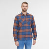 A man with a beard is standing against a plain white background. He is sporting a blue and orange plaid "Shirt Checki Blue 2422-40003-2040" by RAGWEAR, a vegan streetwear cotton flannel shirt with two chest pockets, paired with blue jeans. He is looking straight at the camera with a neutral expression.