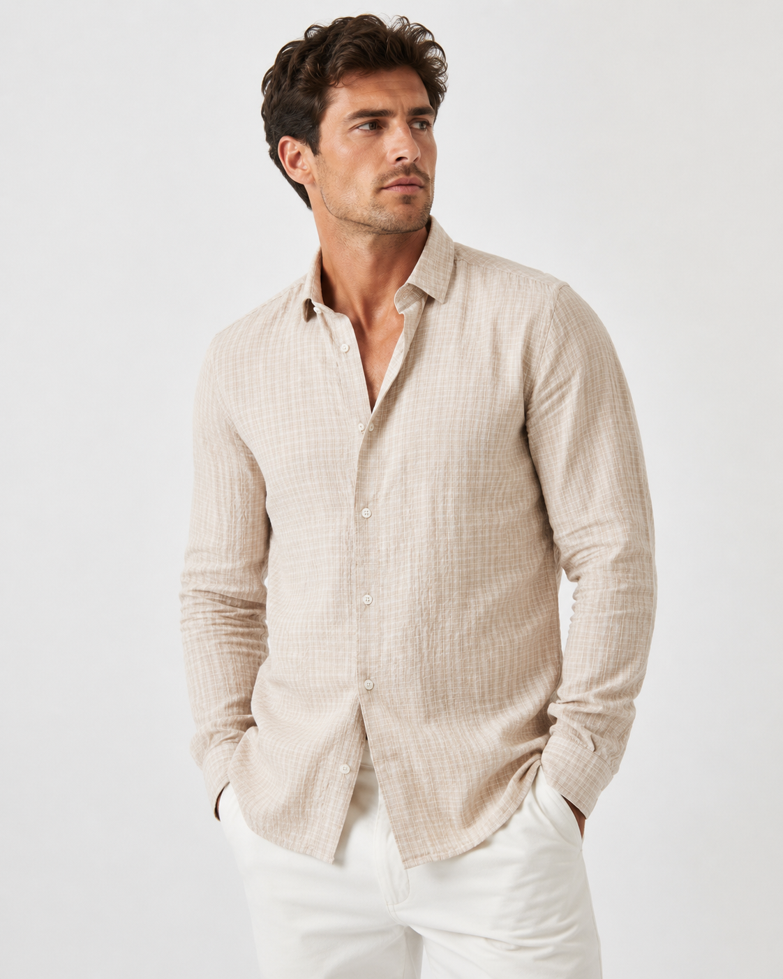 A man wearing a BLEND BARNY SHIRTS 20720753-161104 in light beige with long sleeves and white pants stands with hands in his pockets, gazing slightly to the side against a plain light background.