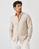 A man wearing a BLEND BARNY SHIRTS 20720753-161104 in light beige with long sleeves and white pants stands with hands in his pockets, gazing slightly to the side against a plain light background.
