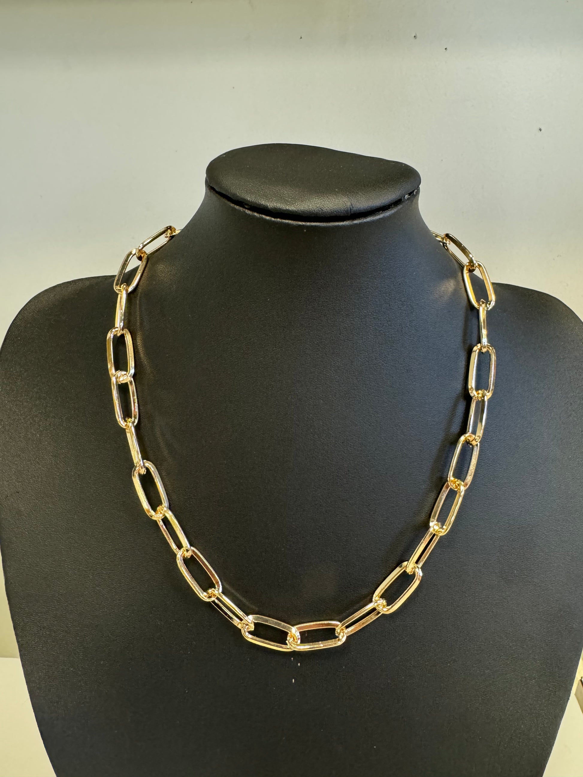 The Rhea 4 Necklace by Elise Accessories is a standout fashion piece, showcasing large rectangular gold links with elegance on a black mannequin bust against a neutral backdrop—an exquisite addition to any jewelry collection.