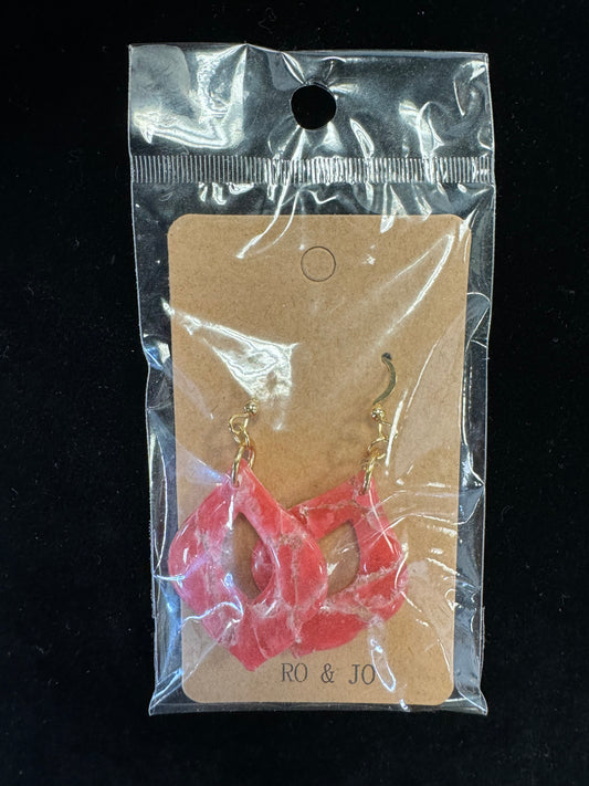 A pair of Ro&Jo Earrings 426, featuring gold-colored hooks and diamond-shaped red resin pendants, is displayed on a brown card inside clear plastic packaging. The card has "RO&JO" printed at the bottom. These unique handmade earrings stand out beautifully against the black background.