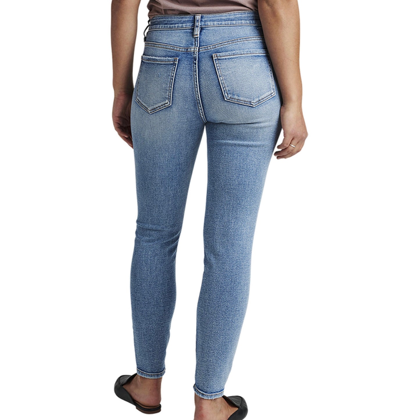 A person is wearing the Cecilia Mid Rise Skinny Jeans by JAG, which are light blue, high-waisted skinny jeans made with power stretch denim and featuring distressed details around the knees and thighs. These jeans have a button and zip closure, belt loops, and pockets. The person is also wearing black, closed-toe shoes and a tucked-in shirt.