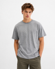 A young man with tousled brown hair wears the RAGWEAR NEDDIS 2512-15002-3000 T-shirt in grey and olive green pants, standing with his hands in his pockets against a light plain background.