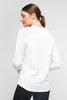 A woman with long brown hair in a ponytail wears a textured white, long-sleeved polyester sweater, paired with black pants. Facing sideways and looking down, the plain light gray background highlights the comfort of her UCHUU-inspired LONG-SLEEVED CREW NECK T-SHIRT CS25-308 ensemble.