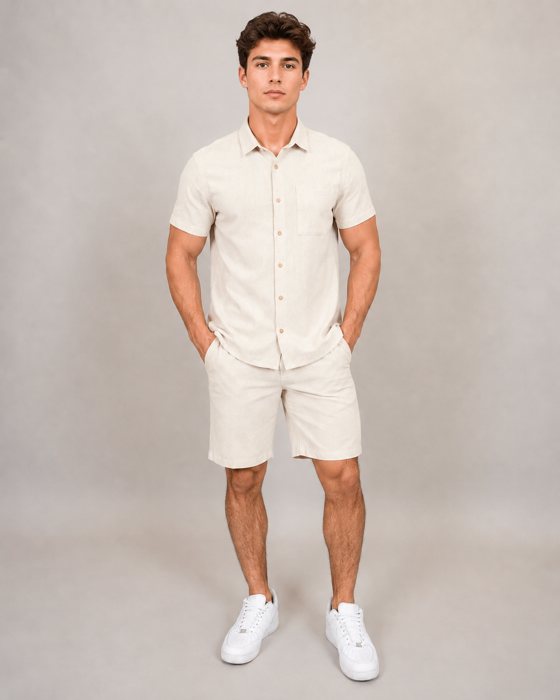 A man stands with hands in pockets, wearing the HEDGE Linen Blend Short Sleeve Button Shirt 56MW104S and matching beige shorts with white sneakers—an ideal warm-weather look—against a plain light grey background.