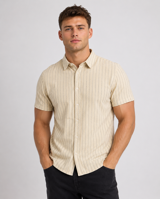 A young man stands against a plain backdrop wearing the BLEND BHAKI SHIRT 20720666-900007166, a short-sleeve cotton-linen shirt with vertical stripes, paired with black pants—effortless summer style from BLEND.