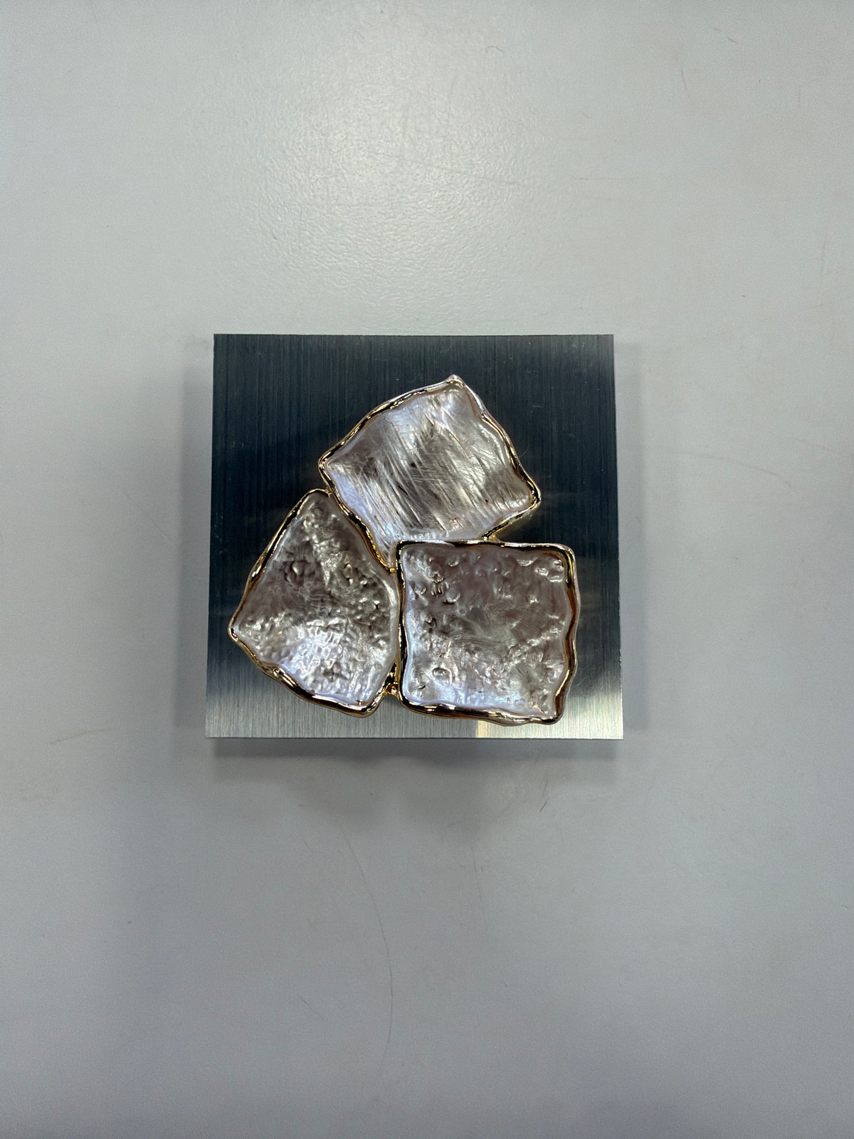 The Elise accessories Denise 26 brooch features three irregular, textured, pearlescent squares with gold edges, mounted on a square brushed metal plate.