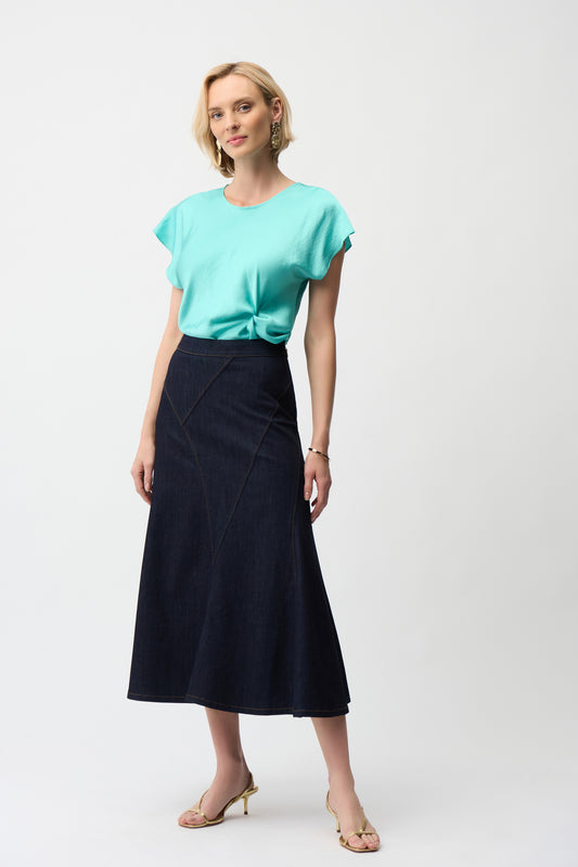 A woman with short blonde hair wears a turquoise tee, beige heeled sandals, and the Joseph Ribkoff Denim Flare Skirt With Exposed Zipper 261969, standing against a plain white background.
