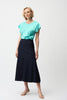 A woman with short blonde hair wears a turquoise tee, beige heeled sandals, and the Joseph Ribkoff Denim Flare Skirt With Exposed Zipper 261969, standing against a plain white background.