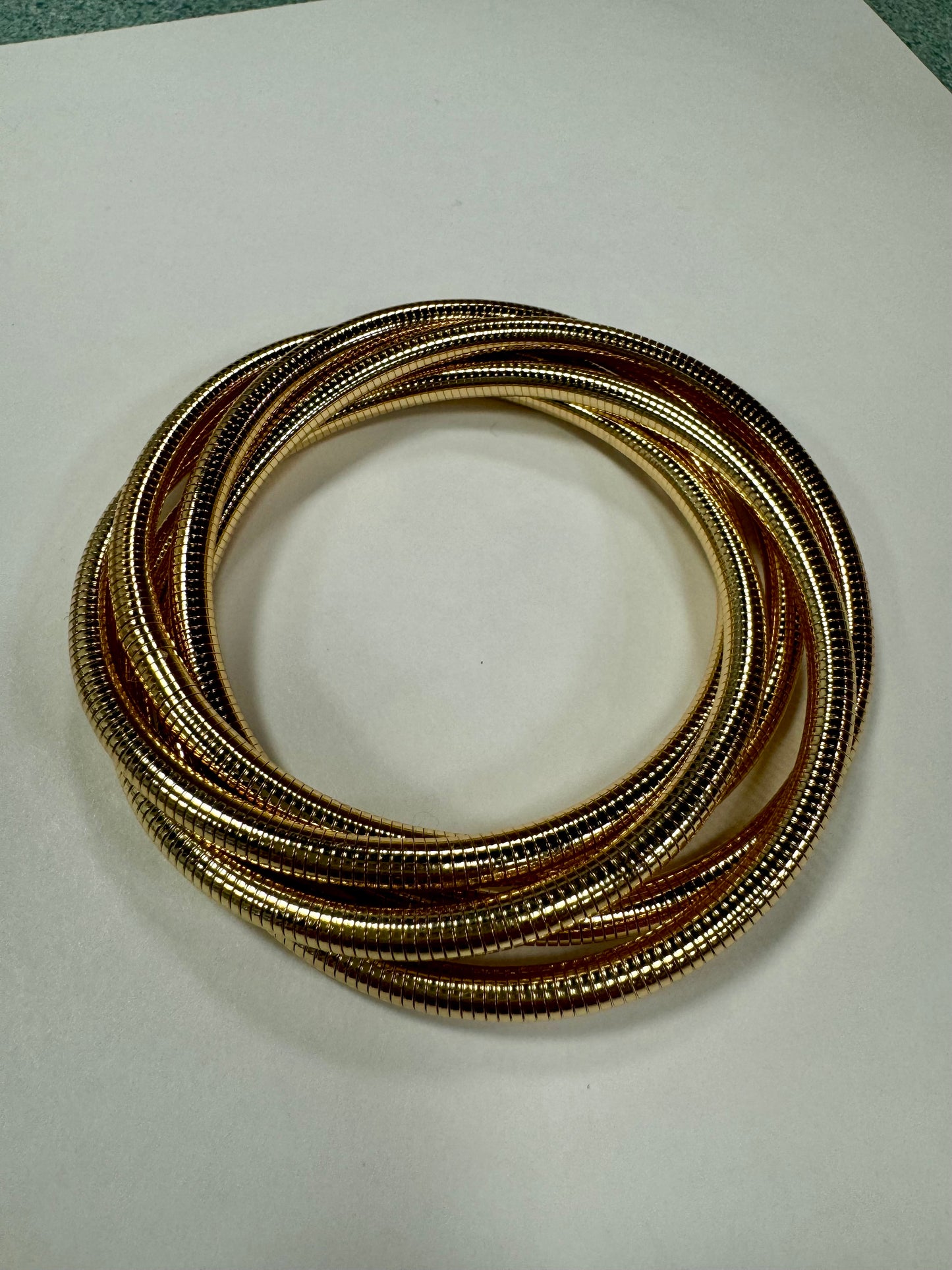 The Gina 36 Bracelet by Elise Accessories showcases an elegant combination of intertwined gold and bronze tones, beautifully arranged in a circular pattern on a white surface.