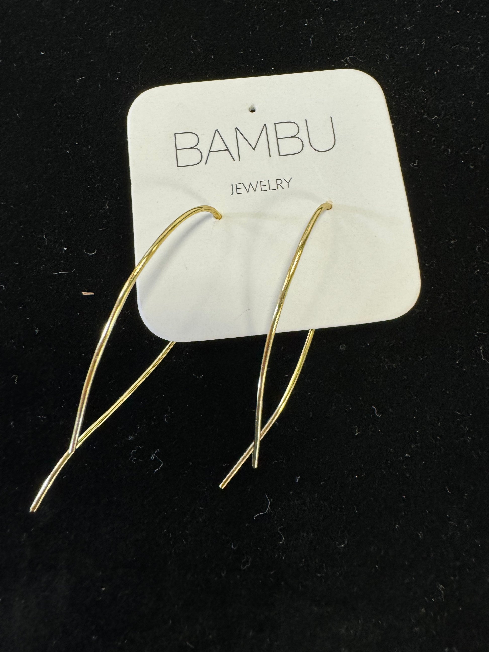 A pair of gold-coloured loop earrings from BAMBU Jewellery, displayed on a white card featuring the brand name "BAMBU Jewellery." The luxury and sophistication of these minimalist, elongated shapes rest beautifully against a black background.