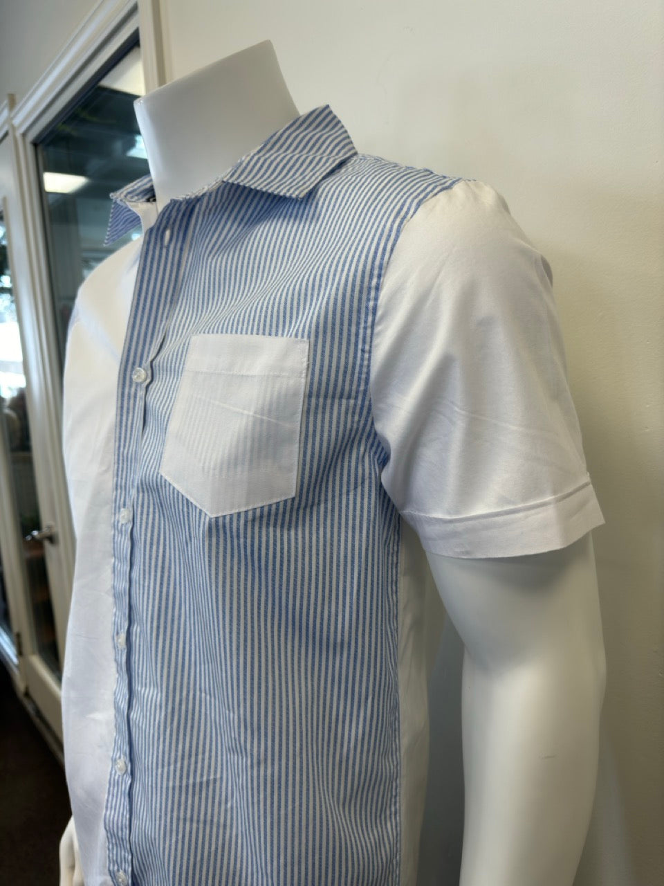 A mannequin showcases the Men’s Cotton Shirt - STRIPE WHITE/BLUE by Silver Jeans Co., which features a button-up style with alternating vertical white and blue stripes on the right side and pocket. The left side and sleeves are solid white, prominently displayed against a plain backdrop that accentuates the garment's unique design.