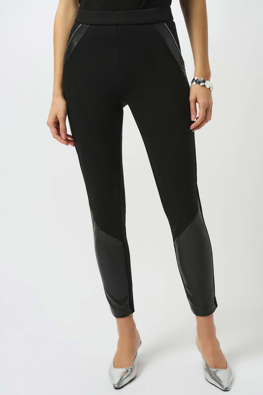 A woman wears Joseph Ribkoff's Heavy Knit and Leatherette Pull-On Legging 253078 with leather-like thigh and calf panels, paired with a bracelet and metallic silver pointed-toe heels, standing against a plain white background.