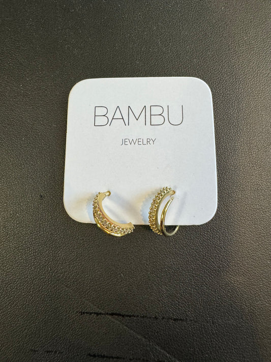 A stunning pair of Gold Embezzled Hoop Earrings from BAMBU Jewellery adorns a white card with "BAMBU JEWELLERY" in gray. These elegant earrings are gold-colored and feature small, clear stones along the front. The card and earrings rest against a dark, textured surface.