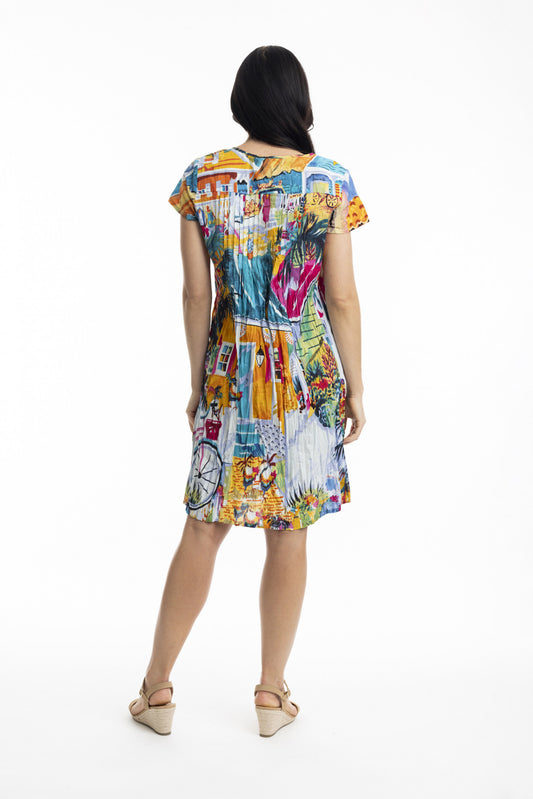 A woman with long dark hair faces away, wearing the ORIENTIQUE Printed Cotton Easy Fit Dress Style: 20058 Florida, featuring a colorful artistic print and V-neckline, paired with beige wedge sandals against a plain white background.