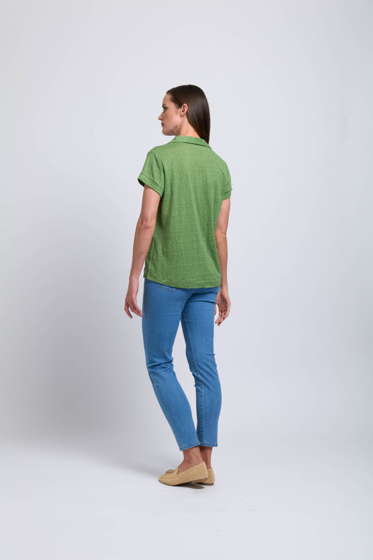 A woman faces away, wearing the FOIL Feature Top CFO7825 -FOIL in green, blue jeans, and beige shoes—an effortless summer outfit—set against a plain white background.