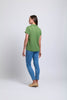 A woman faces away, wearing the FOIL Feature Top CFO7825 -FOIL in green, blue jeans, and beige shoes—an effortless summer outfit—set against a plain white background.
