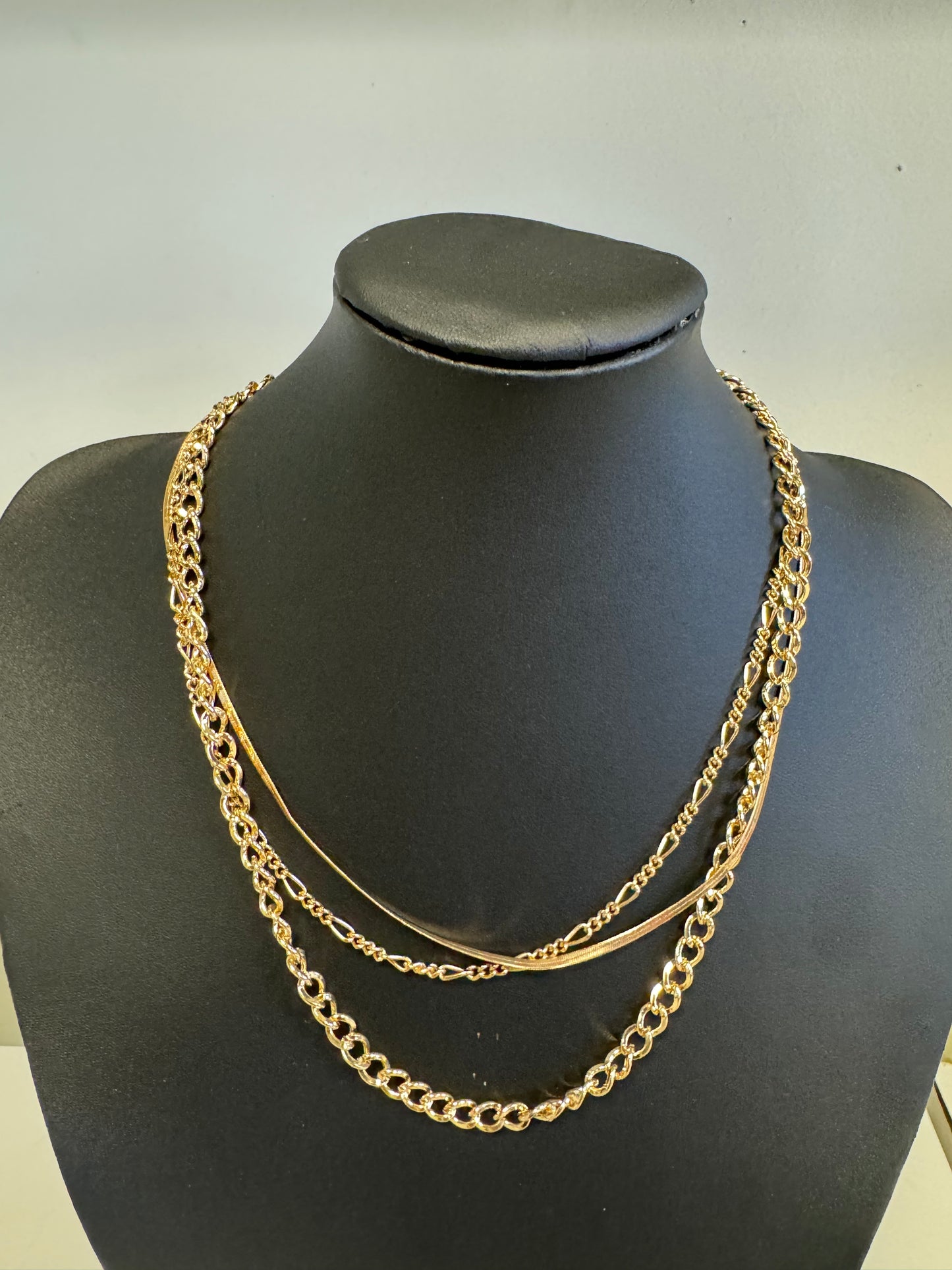 The Chain Necklace from Elise Accessories, elegantly displayed on a black mannequin bust, boasts multiple layered chains of varying thicknesses, exuding an elegant and stylish look. Its versatility ensures it stands out in any jewelry collection, with the neutral background enhancing its allure.