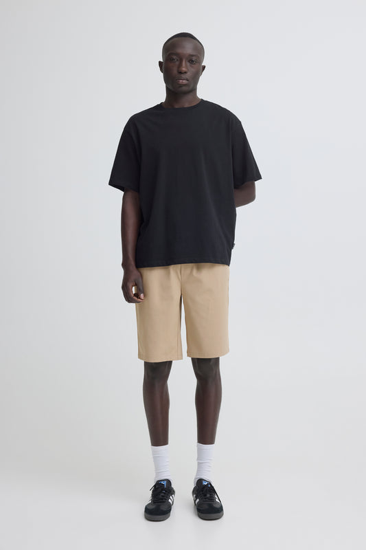 A person stands against a white background wearing a loose black T-shirt, BLEND BHMARCO Regular Easy-pull Wovens Short in beige, white socks, and black sneakers. They have a neutral expression and their left arm is behind their back.