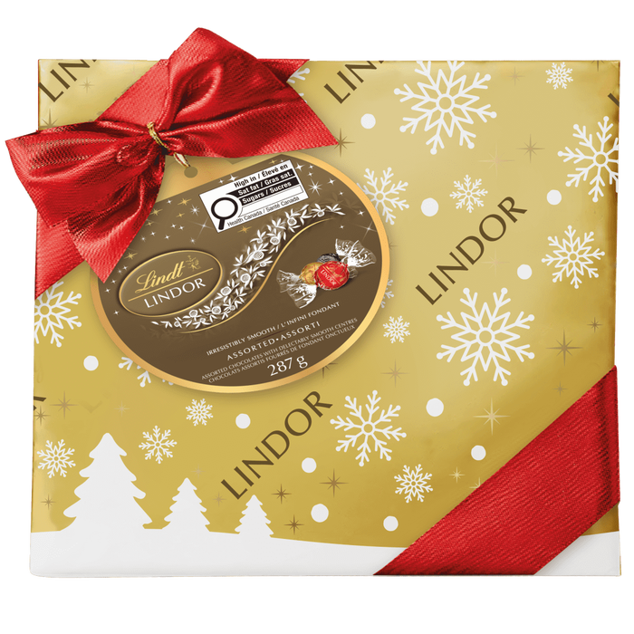 Lindt LINDOR Assorted Chocolate Truffles Gift Box, 287g, features festive white snowflake and tree designs with a red ribbon and bow, plus Lindt Lindor branding and product details.