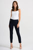 A woman with wavy hair is standing on a plain white background. She is wearing a white sleeveless top, Joseph Ribkoff's Black Pant Style 201483 with an elastic waist, and white strappy heels. Facing the camera with a slight smile, her hands rest by her sides.