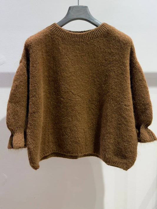 The NOELINE Sweater in kid mohair and wool 5255 in camel, with long sleeves, hangs on a gray hanger against a plain white wall. This fuzzy knit sweater features a loose fit with ribbed cuffs and neckline, delivering both comfort and style.