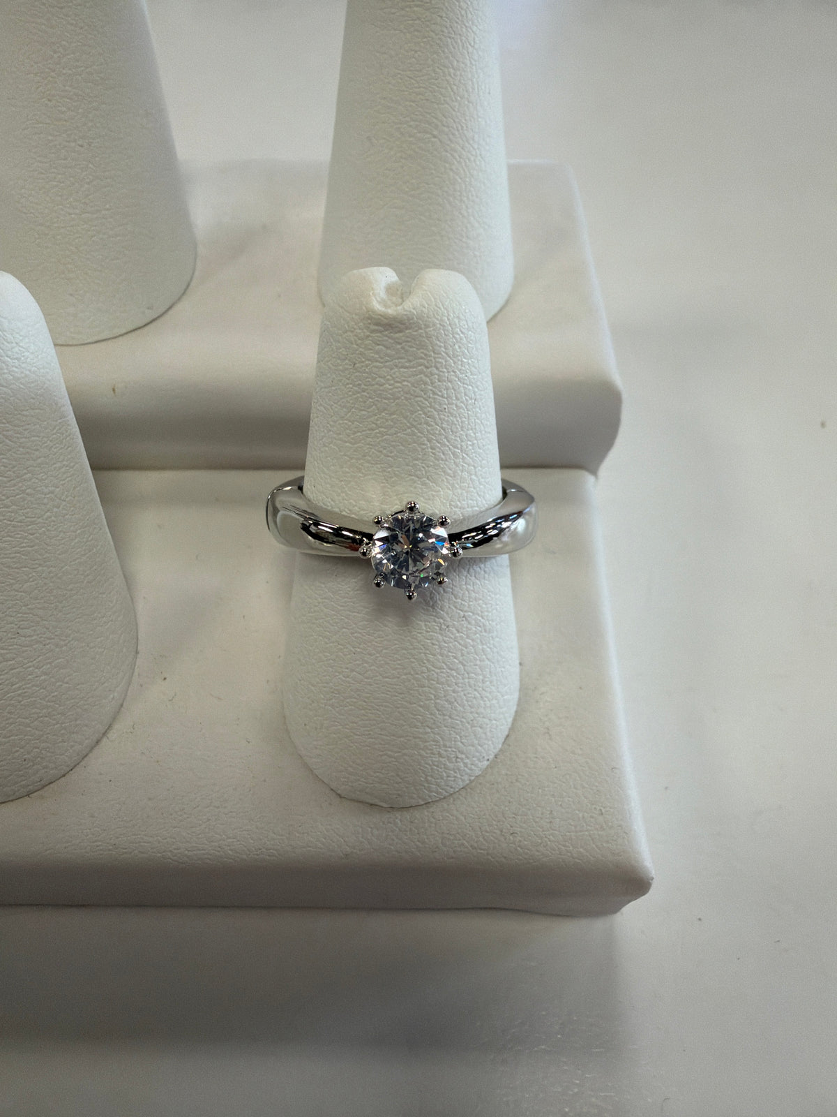 Jenna 64 Ring featuring a CZ solitaire with a round, prong-set gemstone on a polished silver stretch band, displayed on a white ring stand.