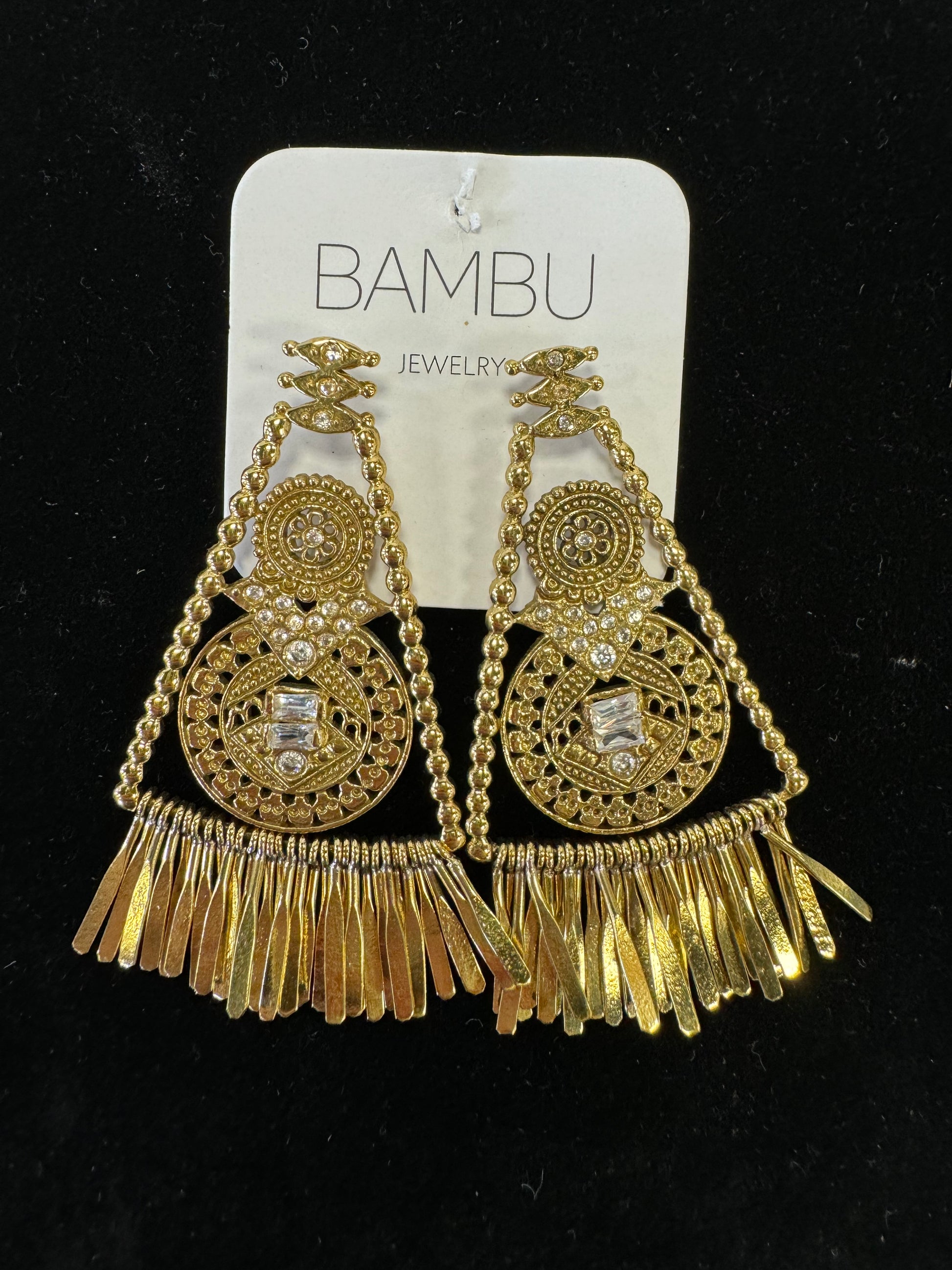 A pair of intricate Golden Jingle Earrings from BAMBU Jewellery, set against a black background. The earrings, featuring circular and triangular designs with detailed patterns, evoke an Egyptian style. Their hanging fringe elements at the bottom create a vintage and elegant look.