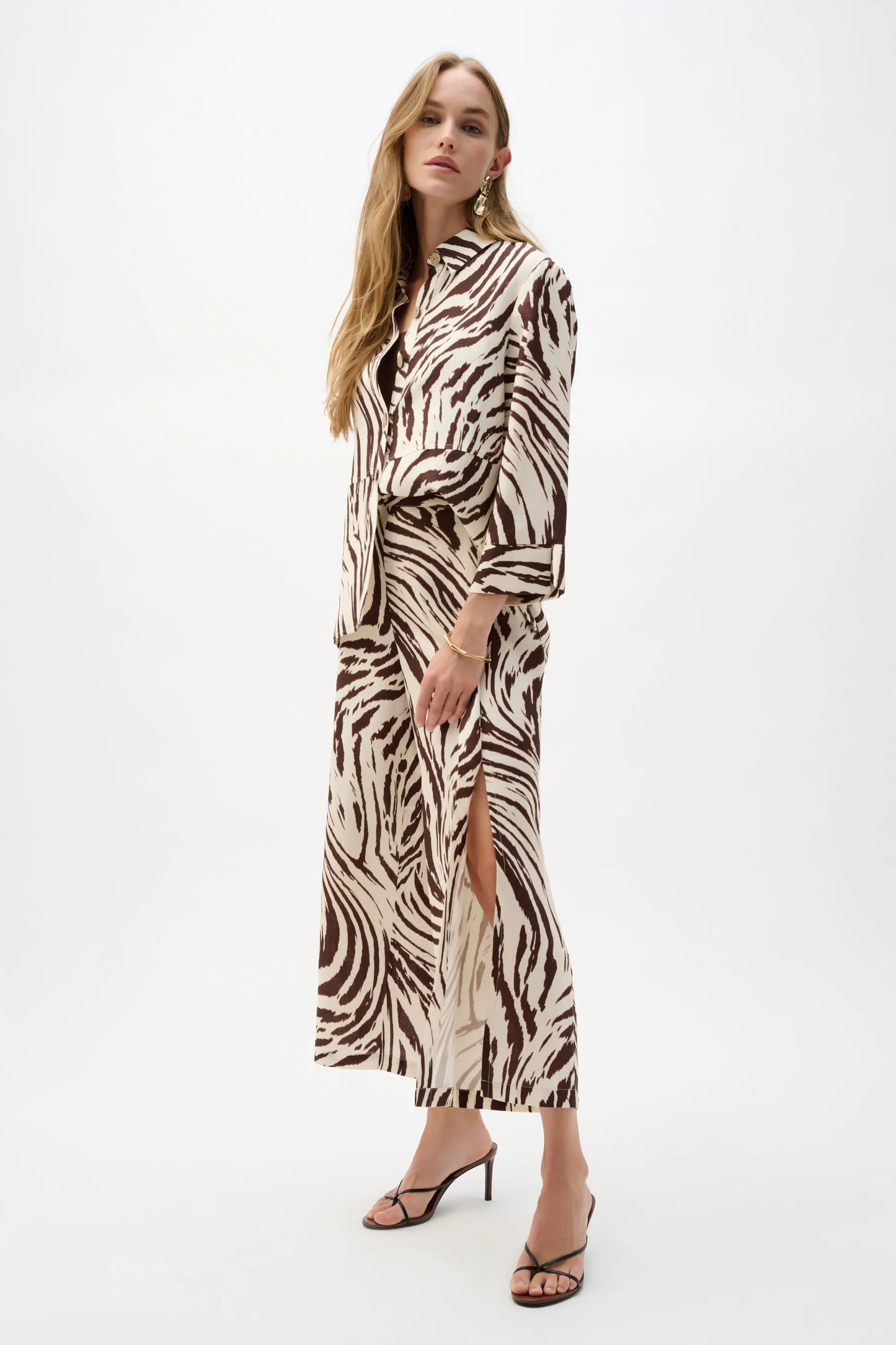 A woman stands against a white background wearing Joseph Ribkoff's Linen Blend Animal Print Culotte Pants With Pleats 262946, featuring an animal print and pull-on waistband, paired with a zebra-print jacket and black heeled sandals.