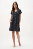 A woman models the Joseph Ribkoff Novelty Abstract Print Trapeze Dress 262170, featuring short dolman sleeves and a V-neckline pleat detail, with one hand in her pocket and the other by her side against a plain white background.