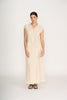 A woman with dark hair pulled back stands against a white background, wearing the FOIL Natural Blender Shell Sandshell FO8474—a lightweight linen-rayon blend button-up top with a matching long skirt featuring frayed hems—and black sandals.