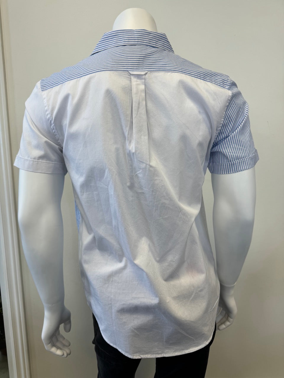 A mannequin showcases the Men’s Cotton Shirt - STRIPE WHITE/BLUE by Silver Jeans Co., which features a button-up style with alternating vertical white and blue stripes on the right side and pocket. The left side and sleeves are solid white, prominently displayed against a plain backdrop that accentuates the garment's unique design.