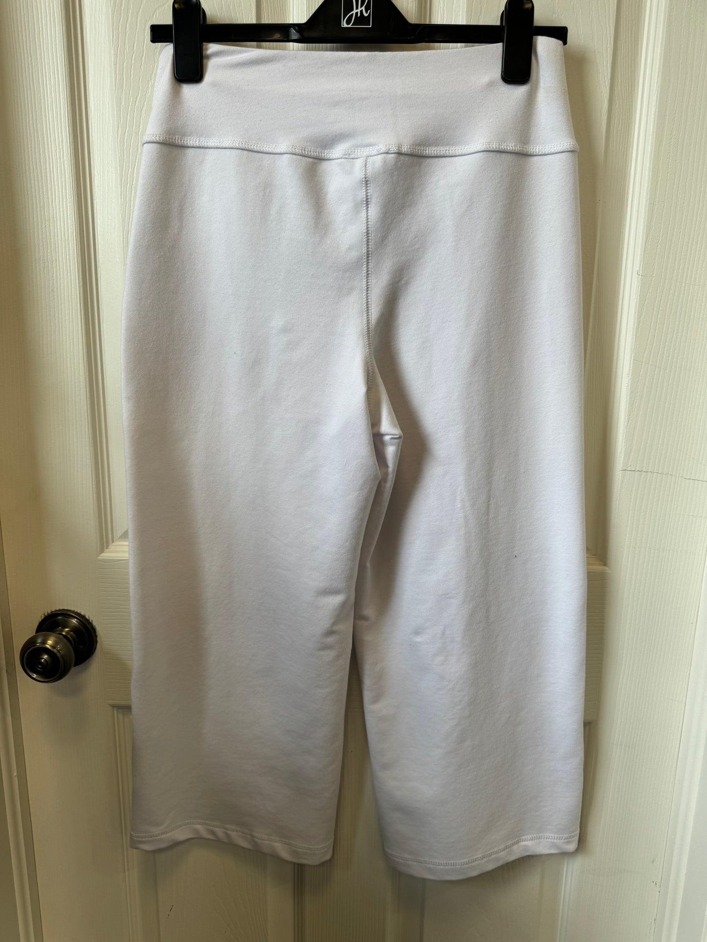 A pair of Tribal White Jogger Pants - 7264O-4532-0001 hangs on a black hanger against a white door. These stylish and functional pants from the Tribal brand feature a high waistband and two large front pockets with a tag attached to one of them. The door has a metallic doorknob on the left side.