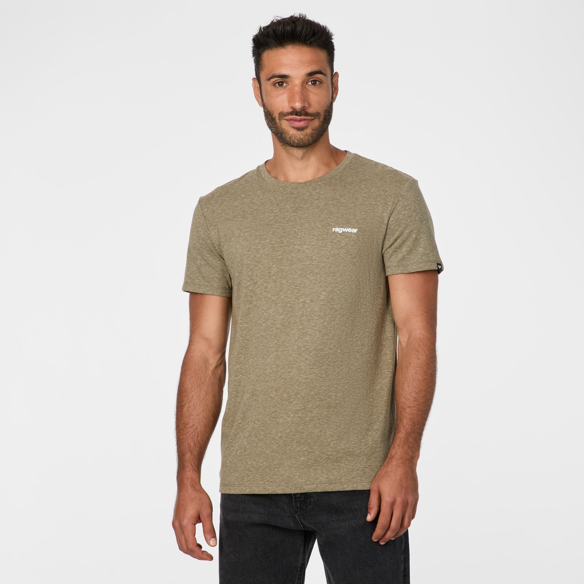 A man with short dark hair and a beard stands against a white background, facing forward in the RAGWEAR Hallys Tee 2612-15004 Dark Olive 5010, paired with black jeans, perfectly showcasing this men's casual tee.