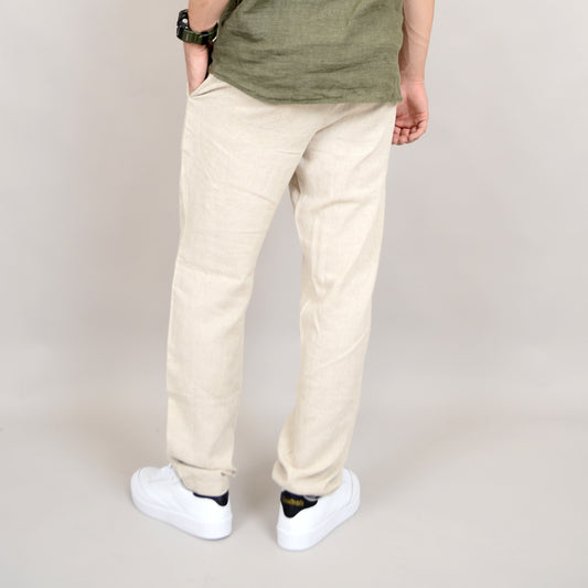 A person stands with their back to the camera, wearing HEDGE Linen Blend Summer Pant 41MW600S in light beige, a green shirt, white sneakers, and a black watch with one hand in their pocket. Ideal for warm weather.