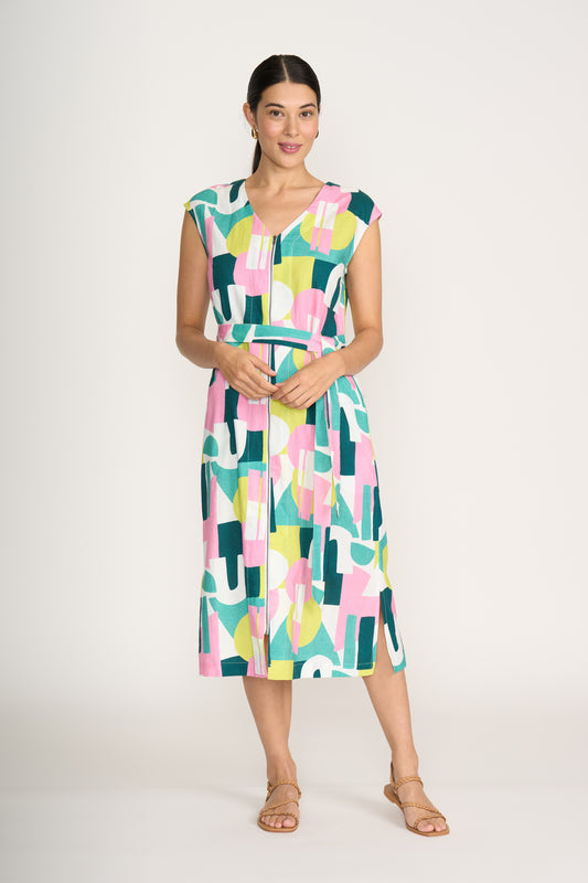A woman wears the FOIL You Little Zipper Dress Spectrum FO8294—a sleeveless, belted midi dress with a geometric pink, green, yellow, and white pattern—paired with tan sandals, standing against a plain white background.