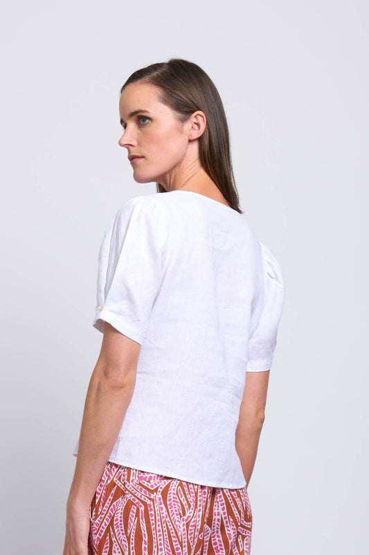 A woman with straight brown hair models the FOIL Good Tuck Shirt FO7800 in white, standing sideways and looking over her shoulder against a plain light background.