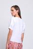 A woman with straight brown hair models the FOIL Good Tuck Shirt FO7800 in white, standing sideways and looking over her shoulder against a plain light background.