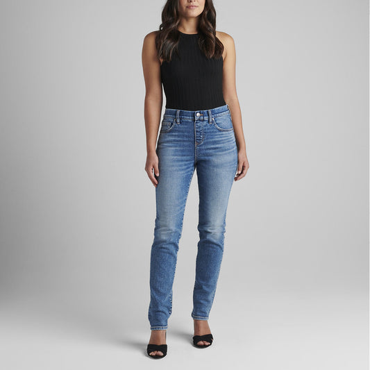 A person stands against a plain gray background, wearing a black sleeveless top and the Valentina High Rise Straight Leg Pull-On Jeans from JAG. They have long, wavy dark brown hair, and are wearing black open-toe heels with their arms relaxed by their sides.