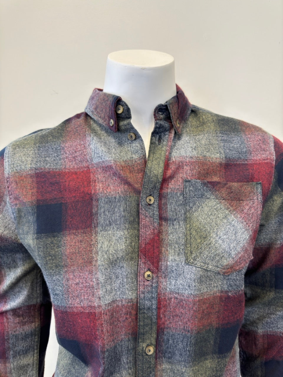 The mannequin is showcasing the Shirt Long Sleeve - BURGUNDY, a button-up flannel with a plaid pattern in shades of red, green, gray, and blue. Expertly paired with denim from Silver Jeans Co., this shirt boasts a single chest pocket and is displayed with the sleeves down and buttons fastened.