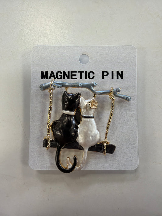The Denise 20 Brooch by Elise accessories depicts a black cat and a white cat sitting together on a swing attached to a branch.