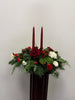 The Double Taper Candle Centrepiece with Roses by Posies Flowers & Fashion features red roses, white blooms, pinecones, greenery, and two tall red candles—ideal as a festive Christmas centrepiece against a white background.